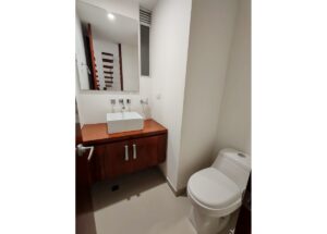 Bathroom with a wooden vanity and square white vessel sink, mirrored cabinet above, and a toilet to the right.