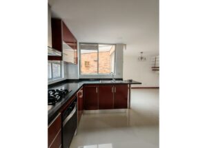 Modern kitchen with dark wood cabinets, stainless steel appliances, and an island sink facing a brick exterior through a large window on the back wall.