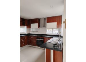 Modern L-shaped kitchen with dark granite counters, wooden cabinets, and a stainless steel stove and oven; an island with a double-basin sink in the foreground.