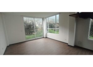 Empty living room with a large glass sliding door and bay windows opening to a green garden outside