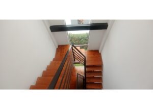 Bird's-eye view of a wooden staircase with a metal railing in a bright white stairwell, leading to glass doors overlooking a garden.