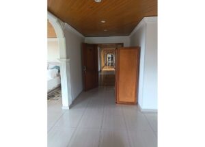 Long interior hallway with a wooden ceiling, archways, and a tall wooden wardrobe on the right; bedroom visible to the left.