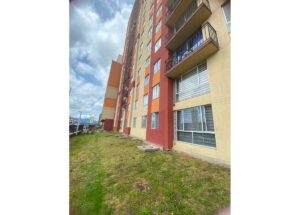 Multistory apartment building with a colorful red, orange, and beige facade and balconies, viewed from a grassy courtyard.