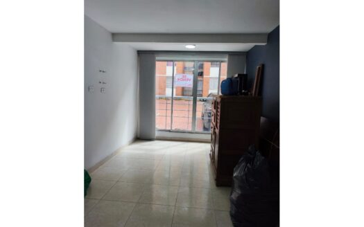 Empty room with tiled floor, a wooden dresser near the sliding glass door, a large black trash bag on the floor, and a street view with a 'Se Vende' sign outside.