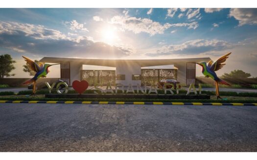 Entrance gate with the word 'YO' and a red heart followed by 'SABANA REAL', flanked by large colorful hummingbirds in front of a sunny sky.