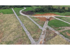 Aerial view of a field with intersecting gravel roads converging at a dirt work area and surrounding green grass.