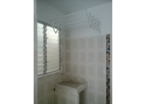 Utility/laundry area with a concrete sink under a louvered window and a wall-mounted fold-out drying rack above, tiled walls with a slim mosaic border on the right edge.