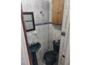Small bathroom with a green pedestal sink and toilet, tiled walls, a wall mirror, and a wooden cabinet above the toilet.