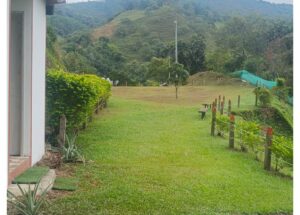 Lawn path toward a small tree and bench, with a rope fence on the right and mountains in the background, left by a building edge.