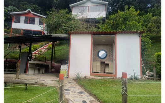 Small white utility building with a circular window and beige cabinets inside, on a grassy hillside; a stone walkway and rope fence lead to it.