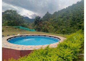 Round blue swimming pool surrounded by a stone patio with green hills and cloudy sky in the background