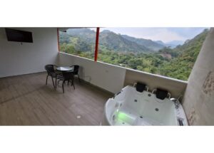 Outdoor balcony with a white hot tub and a small round table with four black chairs, overlooking green mountains.