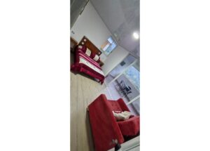 Bedroom with burgundy bedding and a red sofa, plus a balcony with a small table and chairs visible through glass doors