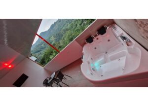 White outdoor hot tub with jet seats on a balcony, red lighting, and a green hillside view beyond.