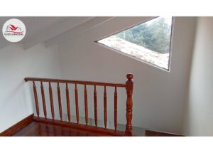Wooden railing with turned balusters along a stairwell, under a slanted triangular skylight window