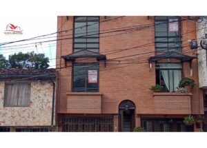 Brick three-story townhouse with rental signs in the windows and a logo in the top-left corner reading 'Nueva Granada Inmobiliaria'