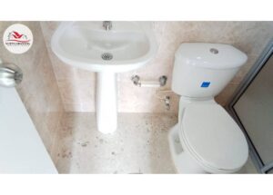 Small bathroom with a white pedestal sink and a toilet; beige tiled walls and floor, with a glass shower on the right.