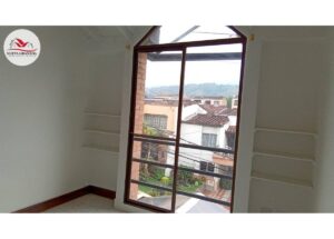 Interior room with a large glass balcony door showing neighboring houses outside; built-in shelves along the walls; watermark logo in top-left corner.