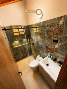Compact modern bathroom with marble walls, glass shower enclosure, white toilet, and rectangular sink on a wooden vanity