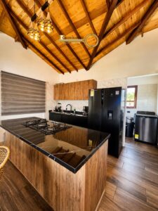 Modern kitchen with a wood-framed vaulted ceiling, hanging pendant lights, and an island with a gas cooktop and black marble countertop.