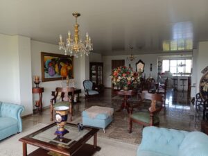 Vintage living room with blue upholstered chairs, a glass coffee table, and a large floral centerpiece on a round wooden table.