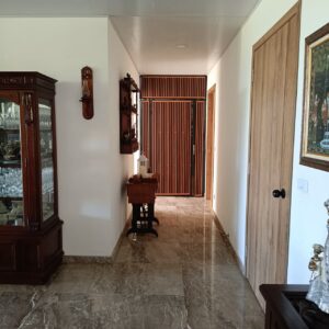 Wide hallway with marble floor and wooden furniture, leading to a slatted wooden gate at the end.