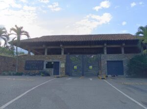 Gated stone entrance to Colinas de Nir Avalle, with a tile-roof building behind and palm trees on either side under a blue sky.