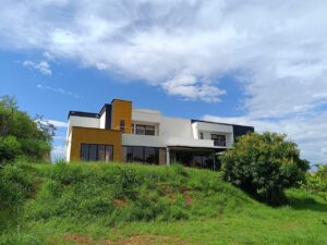 Modern two-story house on a grassy hill under a blue sky with scattered clouds.