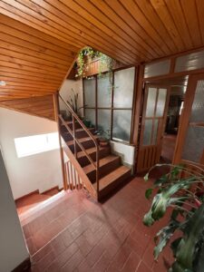Interior stairwell with wooden paneling, brown tiled steps, and a glass-block wall; potted plants on the landing near a wooden door frame.