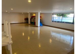 Spacious empty basement playroom with a colorful plastic playhouse and slide in the back corner.