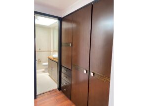 Tall dark wood built-in wardrobes with drawers beside a doorway to a bathroom containing a sink and toilet in a tiled room