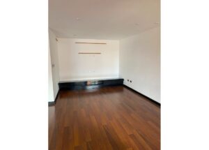 Empty room with dark wood floors and white walls; a long black base cabinet runs along the back wall with two slim wooden shelves mounted above and electrical outlets below.