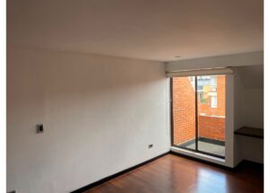 Empty room with white walls, dark wood floor, and a large sliding glass door opening to a brick exterior balcony. It has a small built-in shelf on the right.